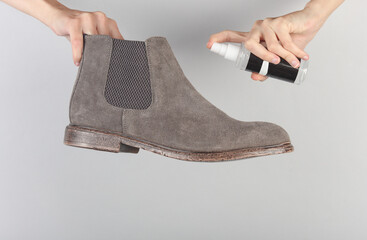 Hands applying water-repellent spray to suede Chelsea boots on a gray background. Shoe care