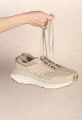 Female hands holding sports sneakers on a beige background