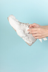 Hand holds white sneaker with cleaning foam on a blue background. Shoe care