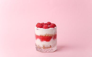 Homemade layered Dessert in a glass cup with yogurt and raspberries on a pink background