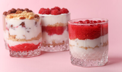 Homemade layered Desserts in a glass cups with yogurt, berries, cookie and chocolate on a pink background