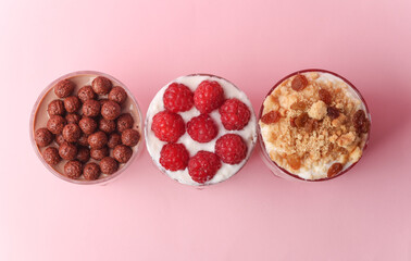 Homemade layered Desserts in a glass cups with yogurt, berries, cookie and chocolate on a pink background. Top view