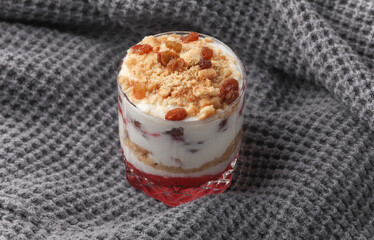 Homemade layered Dessert in a glass cup with yogurt, jam and cookie on gray fabric blanket