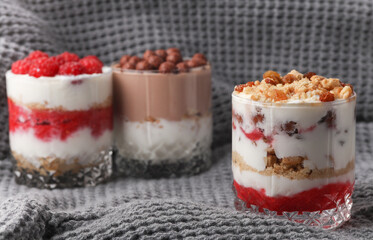 Homemade layered Desserts in a glass cups with yogurt, berries, cookie and chocolate balls on gray fabric blanket