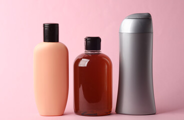 Different shampoo and other cosmetic product bottles on pink background