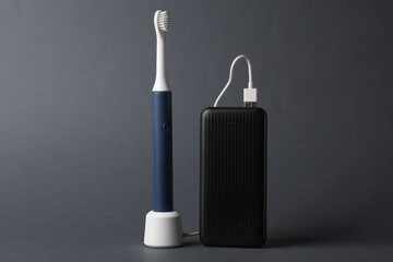 Modern smart ultrasonic toothbrush charging with power bank on dark gray background
