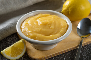 Homemade lemon curd or cream in white bowl, on a gray background.