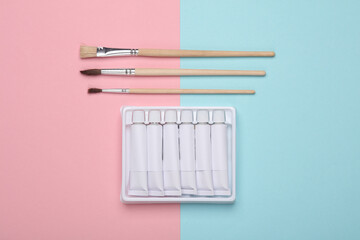 Set of white empty tubes of acrylic or oil paint and brushes for creativity on pink blue background. Template for design, mockup