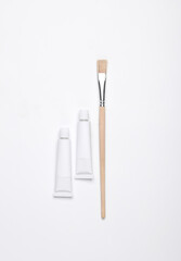 White empty tubes of acrylic or oil paint and brushes for creativity on white background. Template for design, mockup