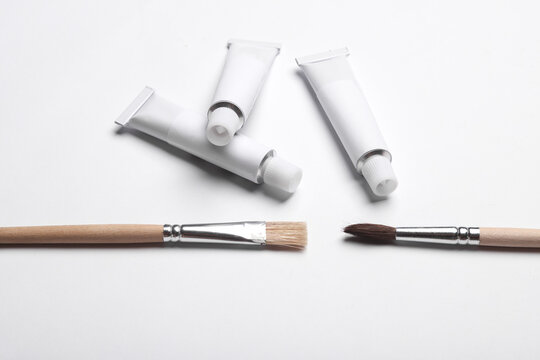 White empty tubes of acrylic or oil paint and brushes for creativity on white background. Template for design, mockup