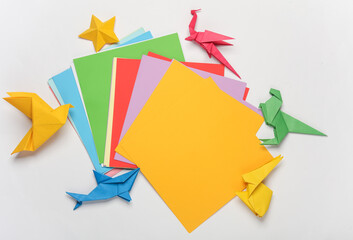 Paper folded origami animal figurines on a white background with colored sheet of papers. Hobbies, creativity