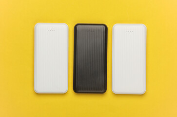 White and black power banks on a yellow background. External batteries for charging smartphone and other gadgets. Top view