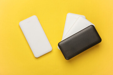 White and black power banks on a yellow background. External batteries for charging smartphone and other gadgets. Top view