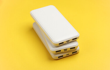 White power banks on a yellow background. External batteries for charging smartphone and other...