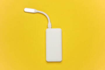 White power bank with cable on a yellow background. External battery for charging smartphone and...