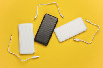 White and balck power banks with cable on a yellow background. External batteries for charging...