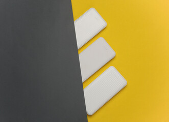 White power banks on yellow background. External batteries for charging smartphone and other...