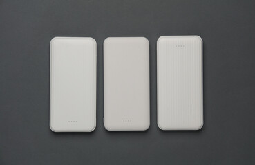 White power banks with cable on dark gray background. External batteries for charging smartphone...