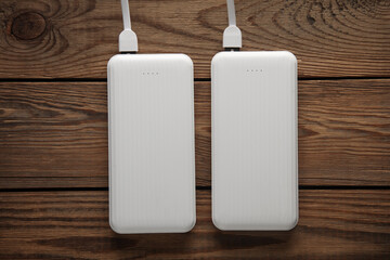 Power banks with cable on wooden table. External batteries for charging smartphone and other...