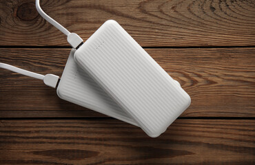 Power banks with cable on wooden table. External batteries for charging smartphone and other...