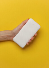 Hand holding white power bank on yellow background