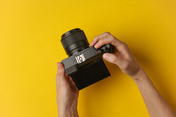Hands holding a modern mirrorless camera on yellow background