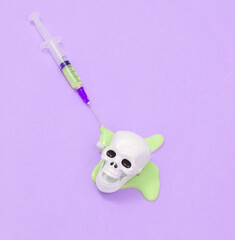 Creative medicine layout. Syringe with slime and skull on purple background. Surreal idea. Conceptual pop
