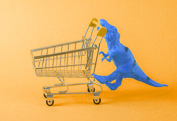 Toy dinosaur tyrannosaurus rex with supermarket trolley on a blue background. Minimalism creative...