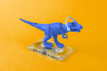 Toy dinosaur tyrannosaurus rex with headphones and audio cassette on yellow background. Minimalism creative layout. Music lover