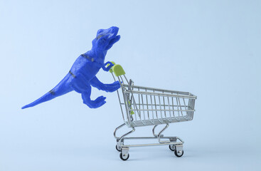 Toy dinosaur tyrannosaurus rex with supermarket trolley on blue background. Minimalism creative layout