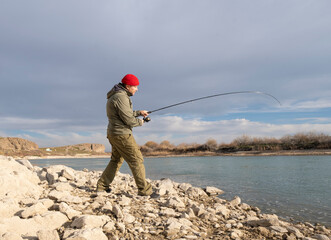 A man catches fish with a spinning rod while standing on the river bank.