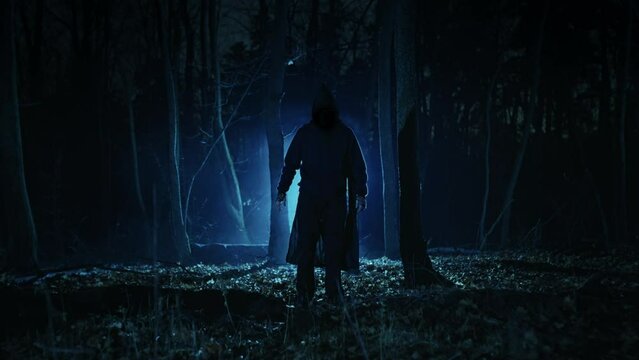A dark figure in a cloak with a hood in a sinister night forest. Fantasy demon or witcher in the night.