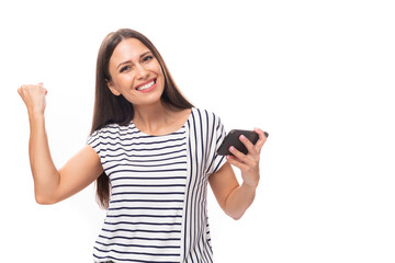 young cheerful energetic caucasian brunette woman in a striped t-shirt holding a smartphone in her hand on a white background with copy space