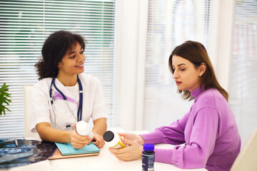 Beautiful young mixed race female doctor with pregnant patient in front of attendee, pill jar holder