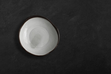 Handmade empty ceramic plate top view with copy space on dark concrete table. Minimalism. Eco friendly ceramics handcraft tableware.