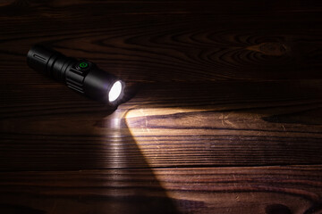 Flashlight and a beam of light in darkness. A modern led lamp with bright projection on dark wood table. - obrazy, fototapety, plakaty