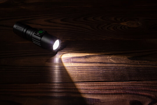 Flashlight and a beam of light in darkness. A modern led lamp with bright projection on dark wood table.