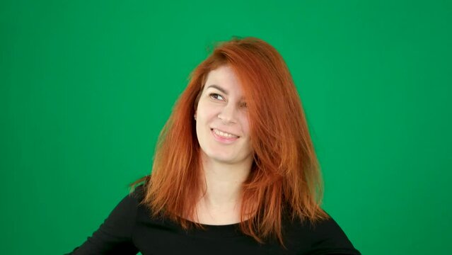 Shaking her head dancing woman with red hair on a green background, laughs, turns her head around, makes dance movements with her shoulders, straightens her hair, chromakey space for text.