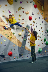 Woman, bouldering trainer teaching child little girl bouldering activity, techniques. Little girl climbing wall, indoor class. Concept of sport climbing, hobby, active lifestyle, school