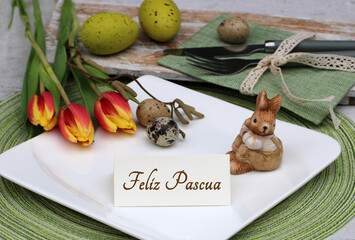 Mesa festiva de Pascua con flores, huevos de Pascua, platos y cubiertos y el texto Feliz Pascua en...