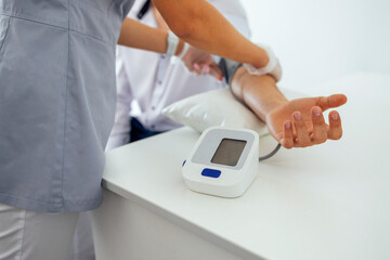 Nurse in medical uniform and transparent gloves checking blood pressure of young man in casual...