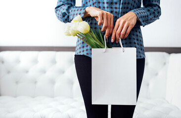 Young beautiful woman closed, halding shop bag with bouquet of tulip flowers.