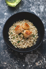 Black bowl with seared scallops and brown rice, vertical shot on a dark-brown granite background