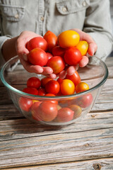 Female hands holding colorful tomatoes over glass bowl on a wooden background.