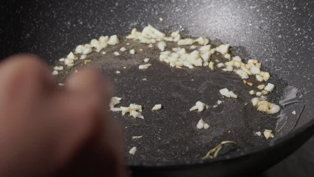 Chef Frying Garlic with Rosemary In Oil On Non-stick Pan. - close up shot