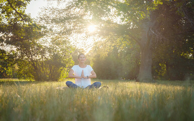 Young asian woman doing meditation in morning or evening at park, healthy woman relaxing and practicing yoga at city park. Mindfulness, destress, Healthy habits and balance concept