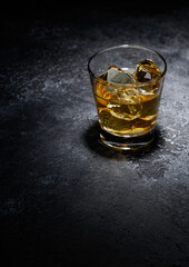 Whiskey glass with ice cubes in middle of black background.