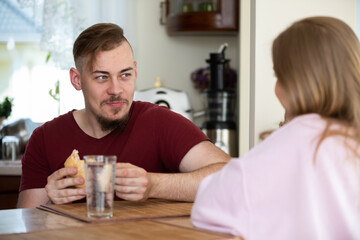 A man sits with his girlfriend in the kitchen and eats breakfast.