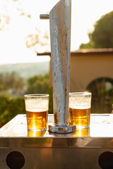 Dispenser with two glasses of beer while the sunlight falls.