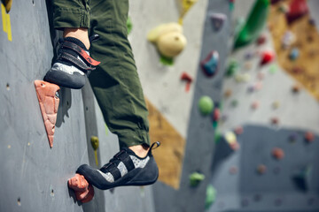 Cropped image of legs in special shoes standing on artificial rock. Bouldering, wall climbing activity . Concept of sport, bouldering, sport climbing, hobby, active lifestyle, school, training course - obrazy, fototapety, plakaty